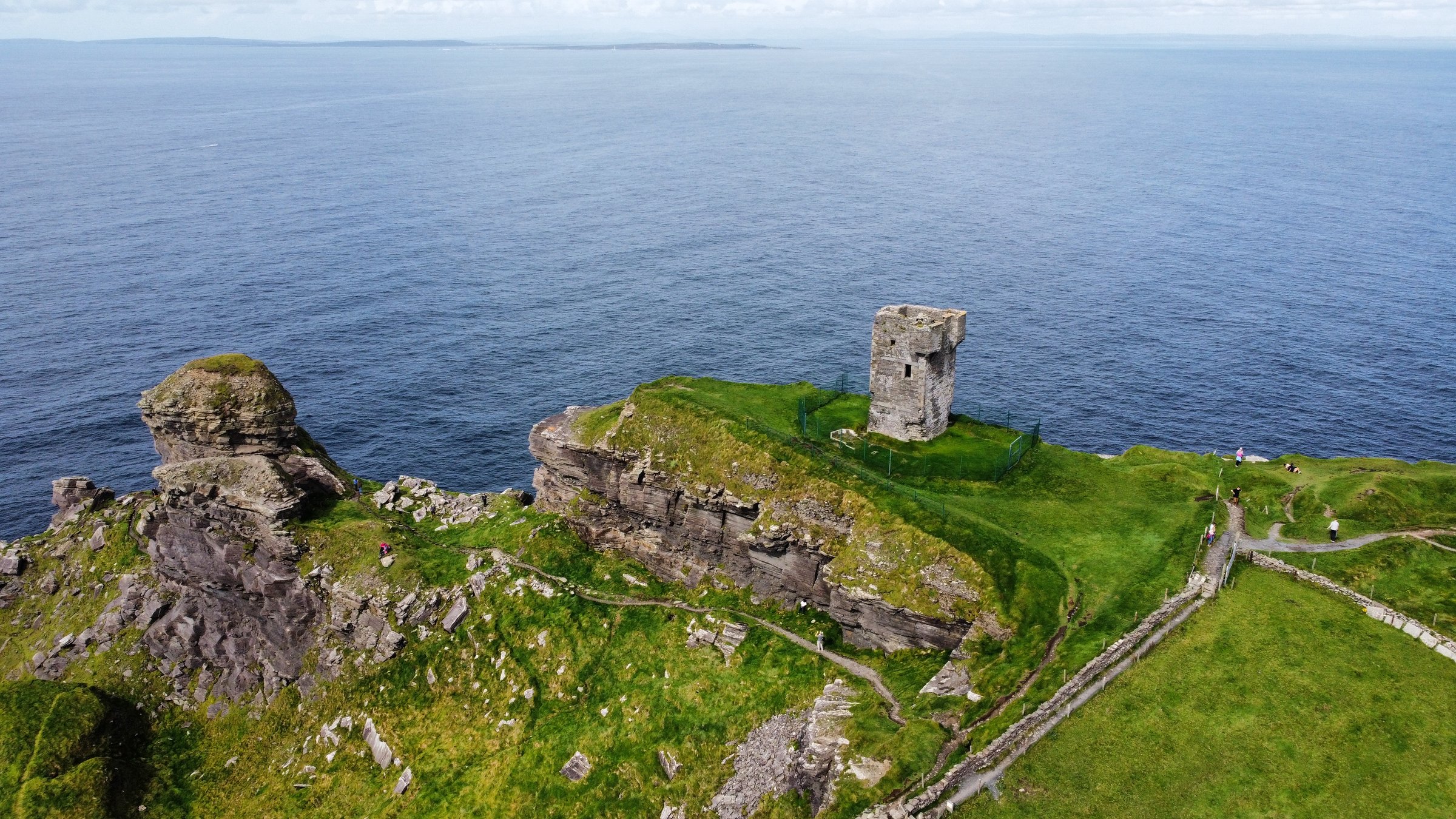 Aerial view of the stone Moher Tower at Hag's Head on green cliffs above the Atlantic Ocean.