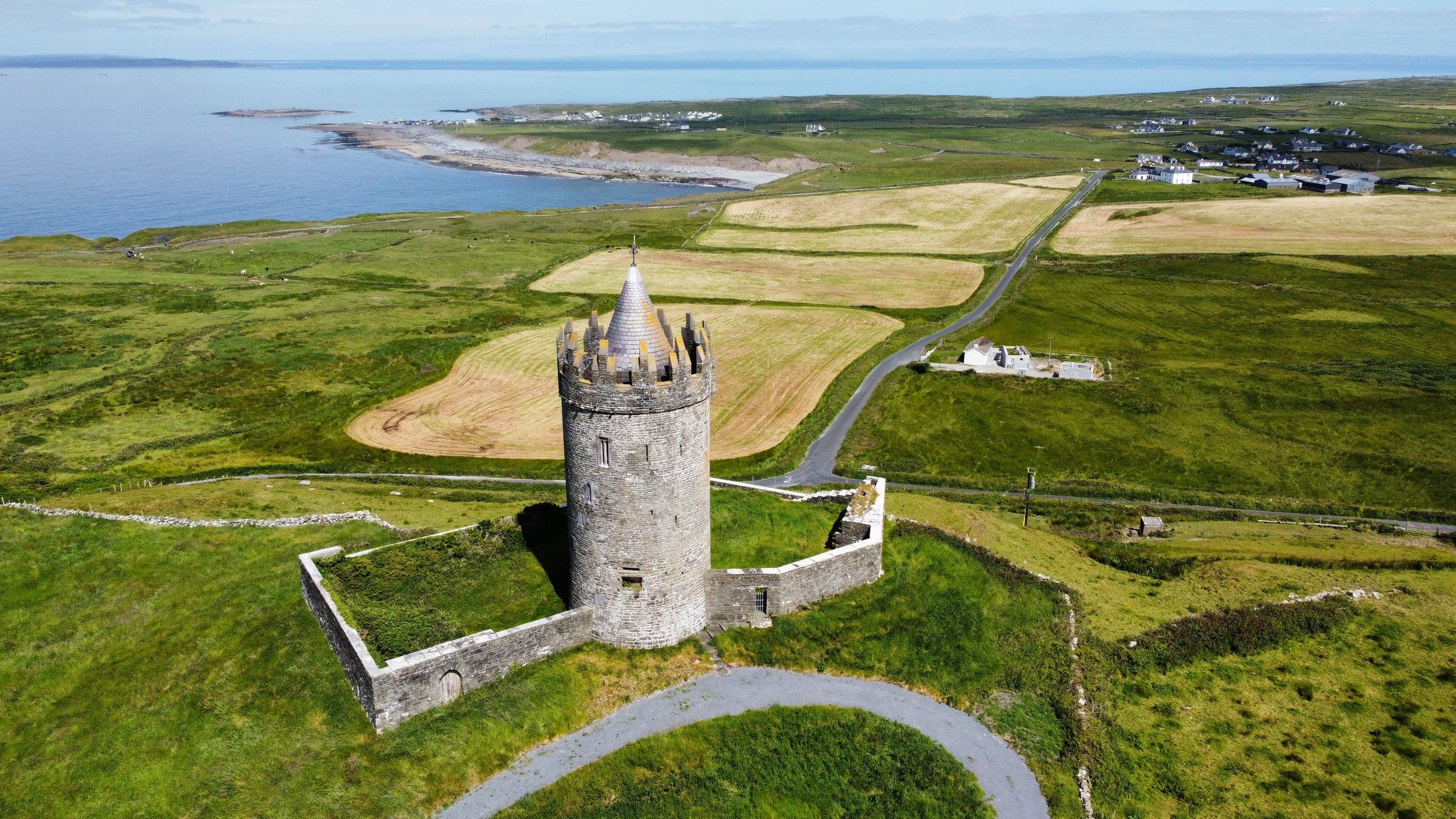 Drone view of Doonagore Castle, a round stone tower on a green hill near the Irish coast.