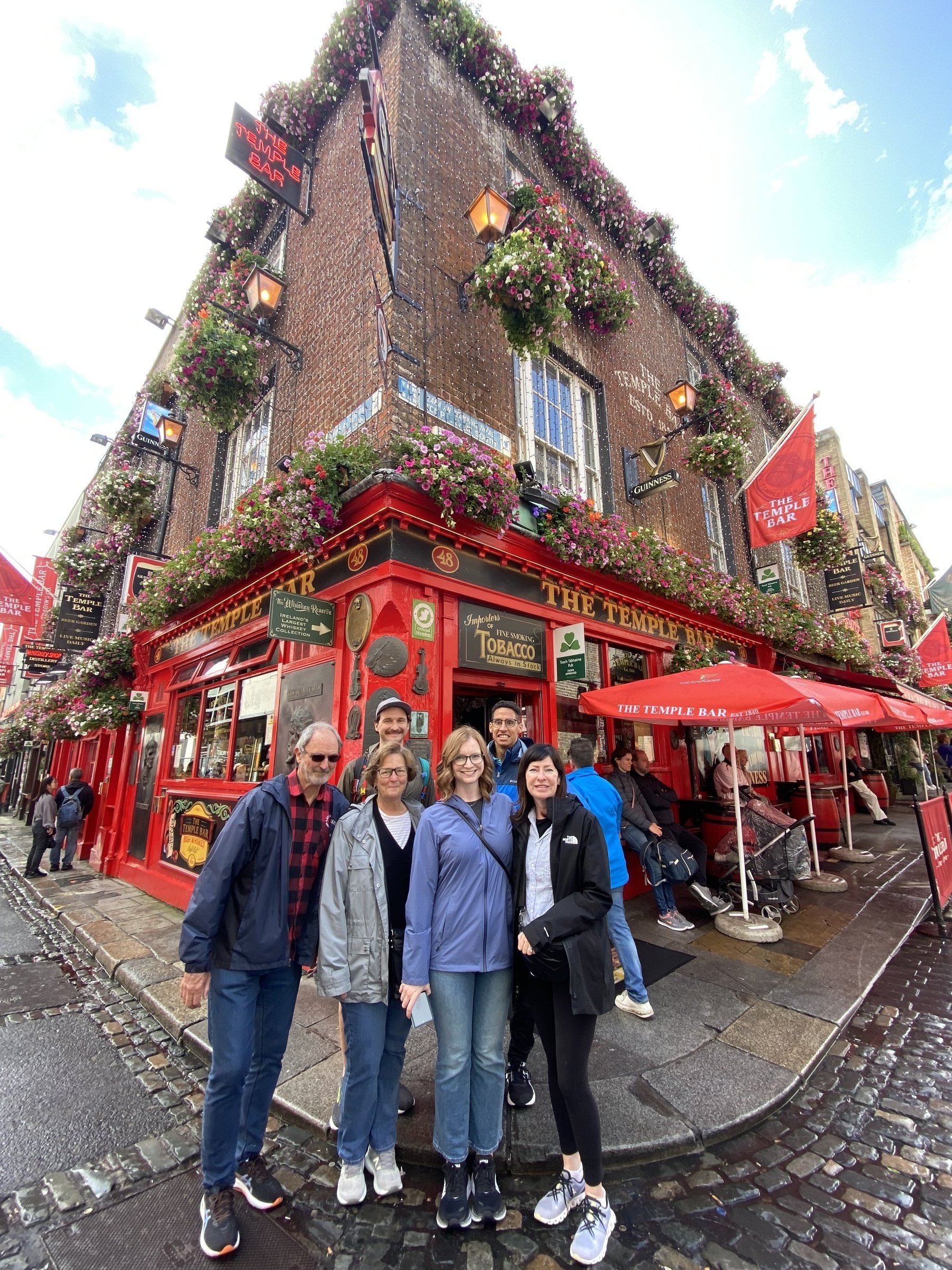 A group of six travelers poses in front of the iconic red facade of The Temple Bar in Dublin.