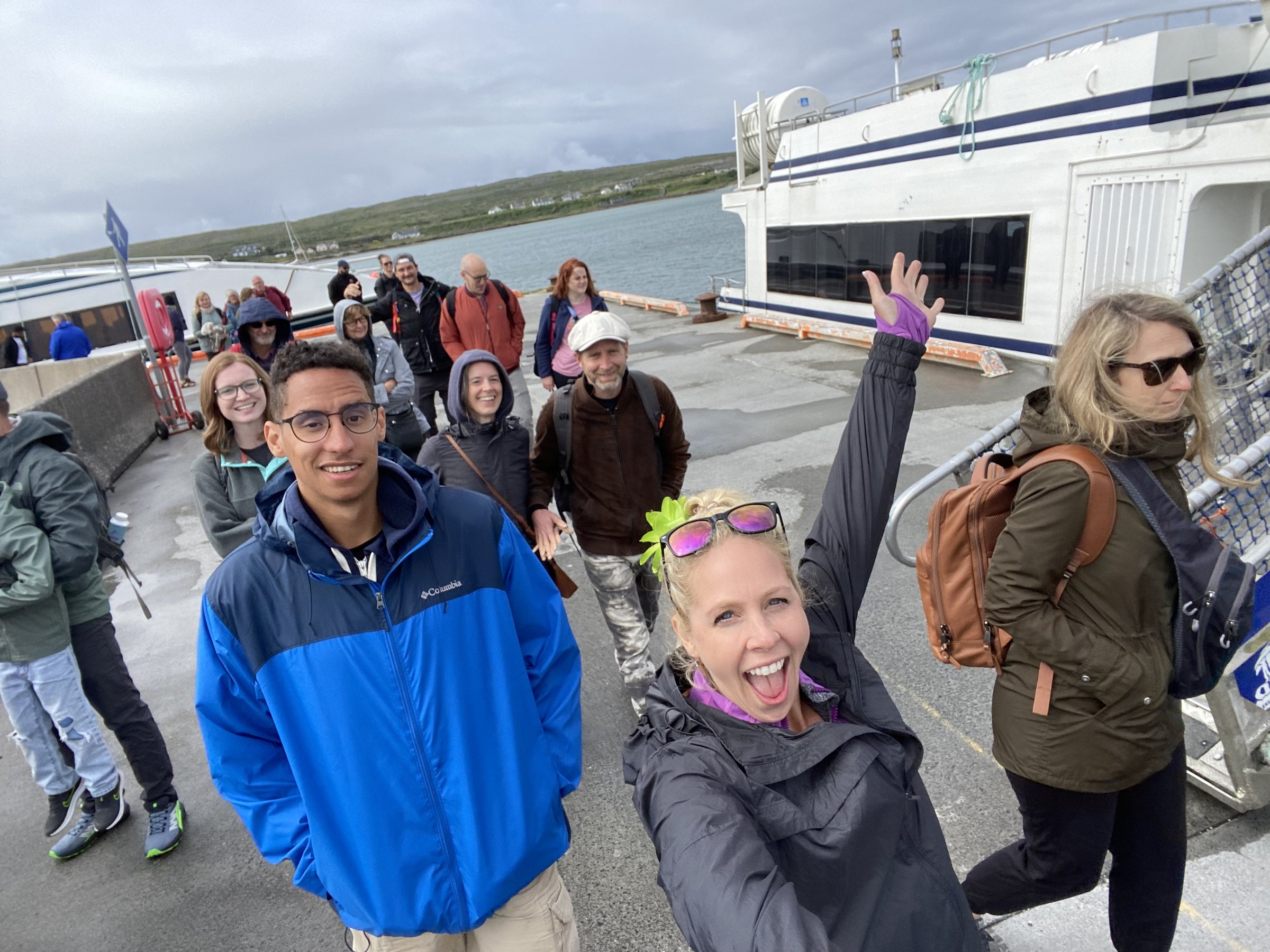 A cheerful group of travelers in outdoor gear gathers on a pier beside a large white ferry.