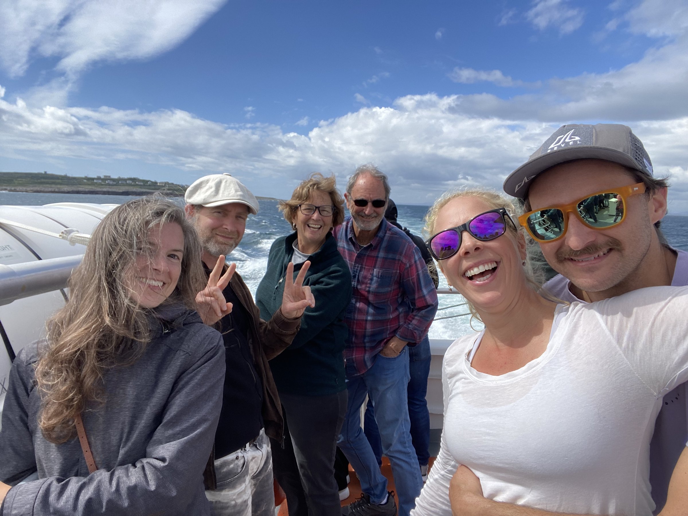 Six smiling travelers pose for a group selfie on the deck of a boat with the ocean behind them.