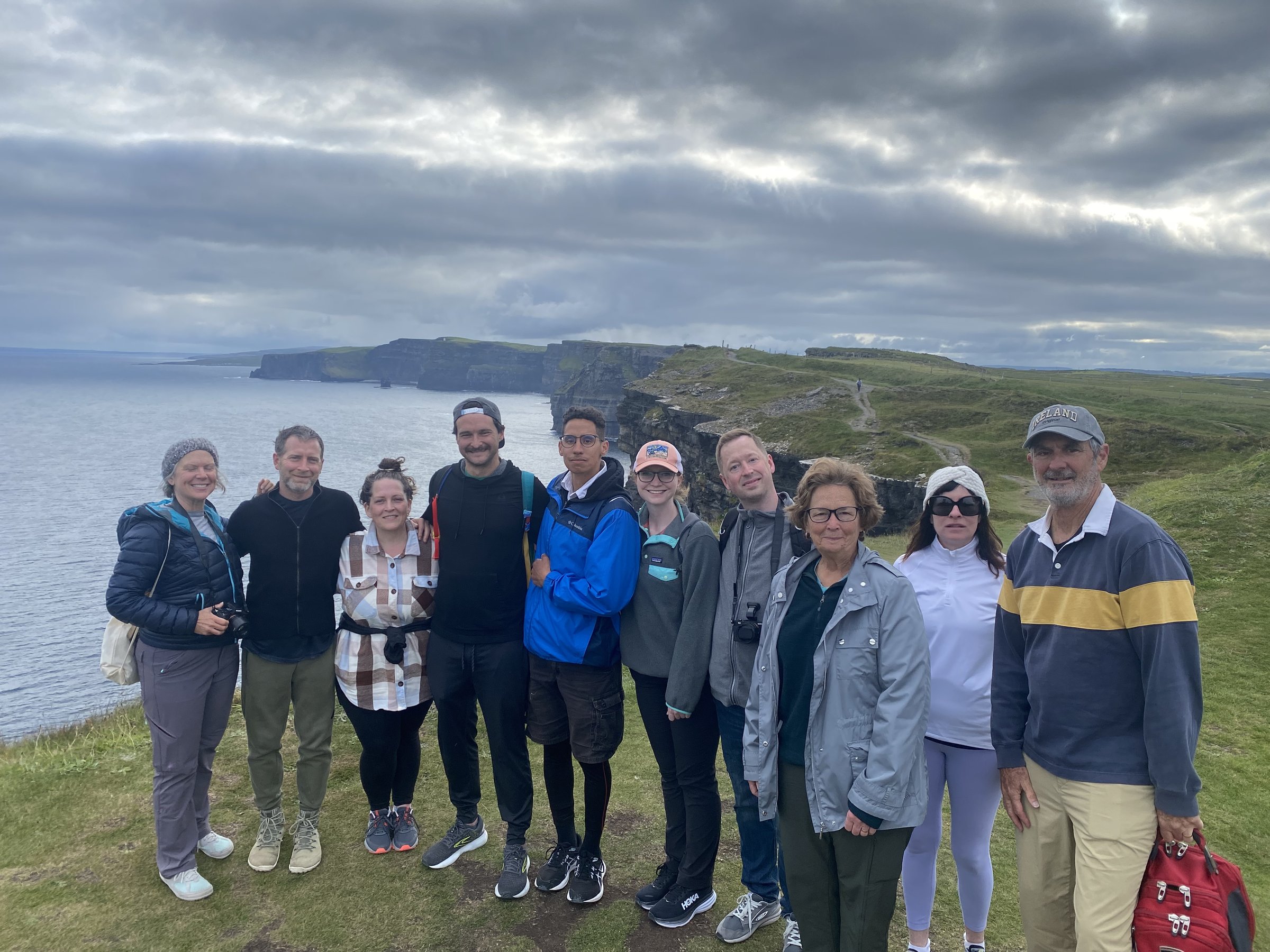 Ten retreat participants pose together on a grassy cliff with the Cliffs of Moher behind them.