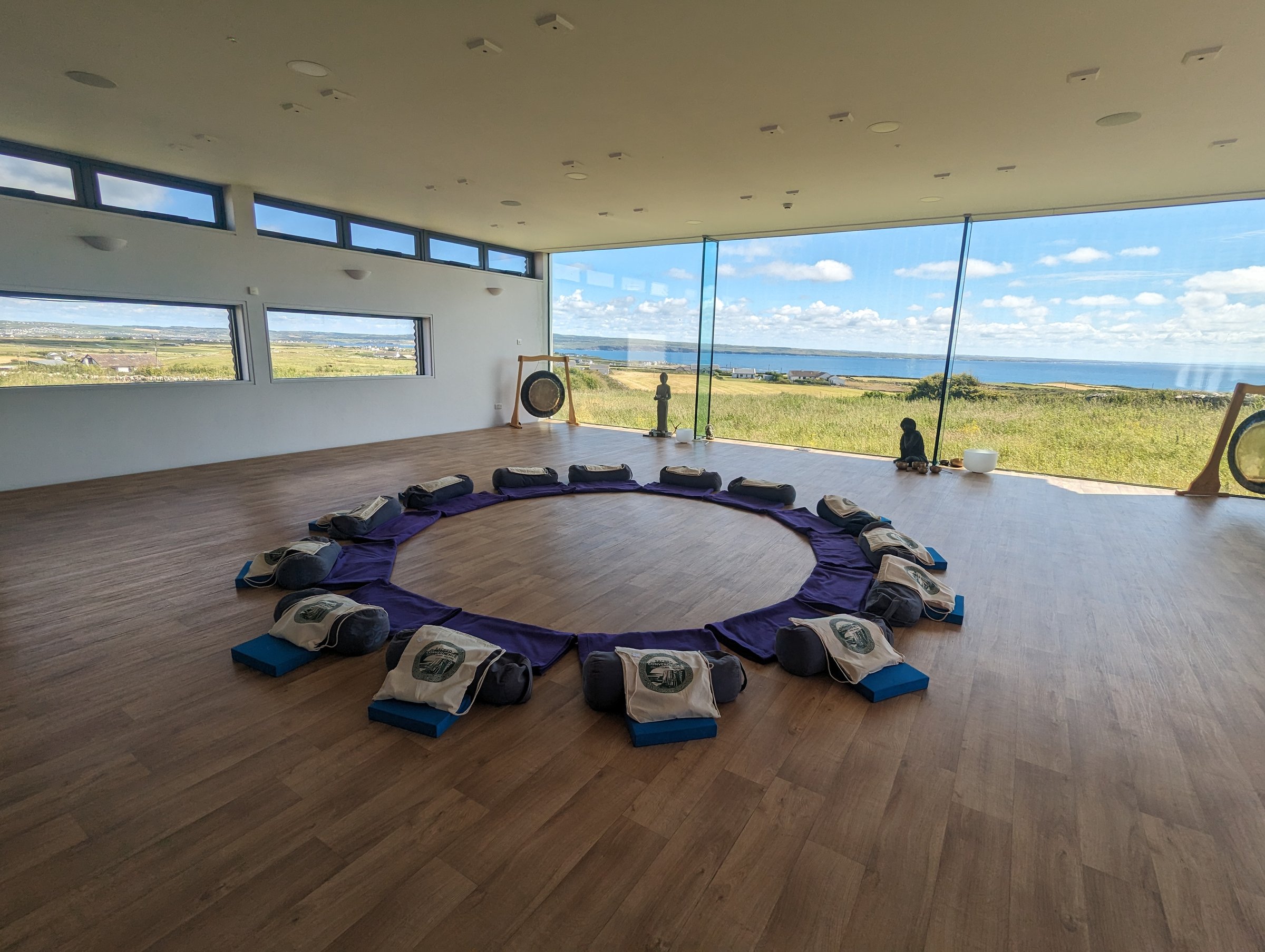 A circle of meditation mats, bolsters, and tote bags in a bright studio overlooking the Irish coast.