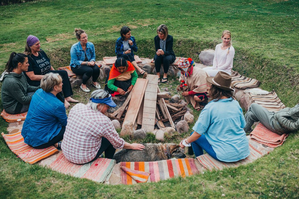 A circle of retreat participants sits on colorful blankets around a stone-lined fire pit during a traditional Andean ceremony in the Sacred Valley.