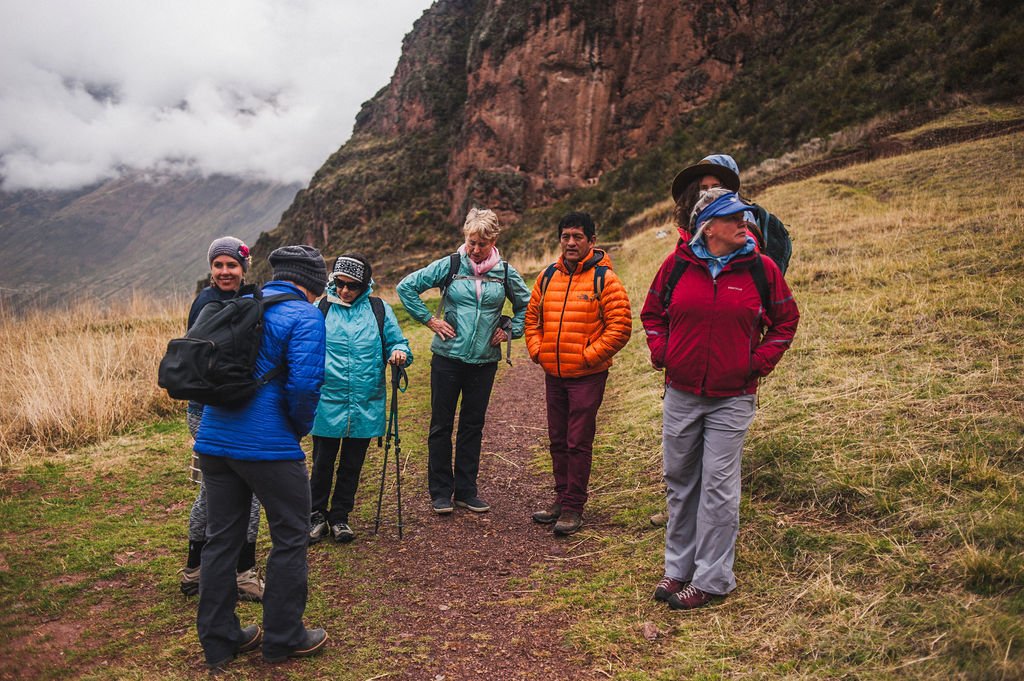 A group of travelers in colorful hiking gear pauses on a mountain trail overlooking a mist-filled valley in the Andes of Peru.