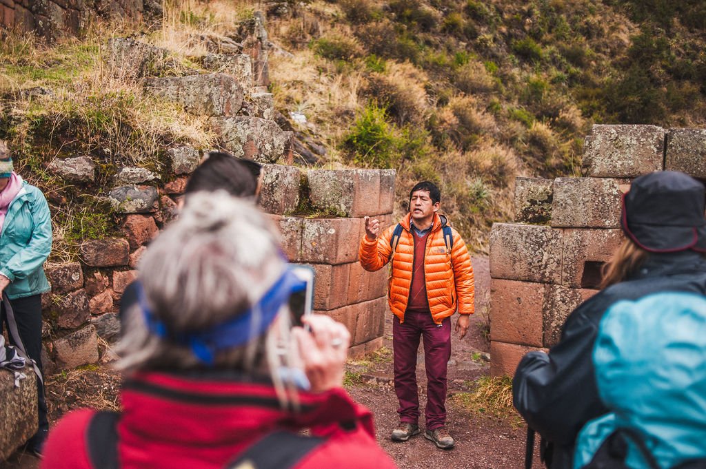 A local guide in an orange jacket explains ancient Inca stone ruins to a group of retreat participants in the Sacred Valley.