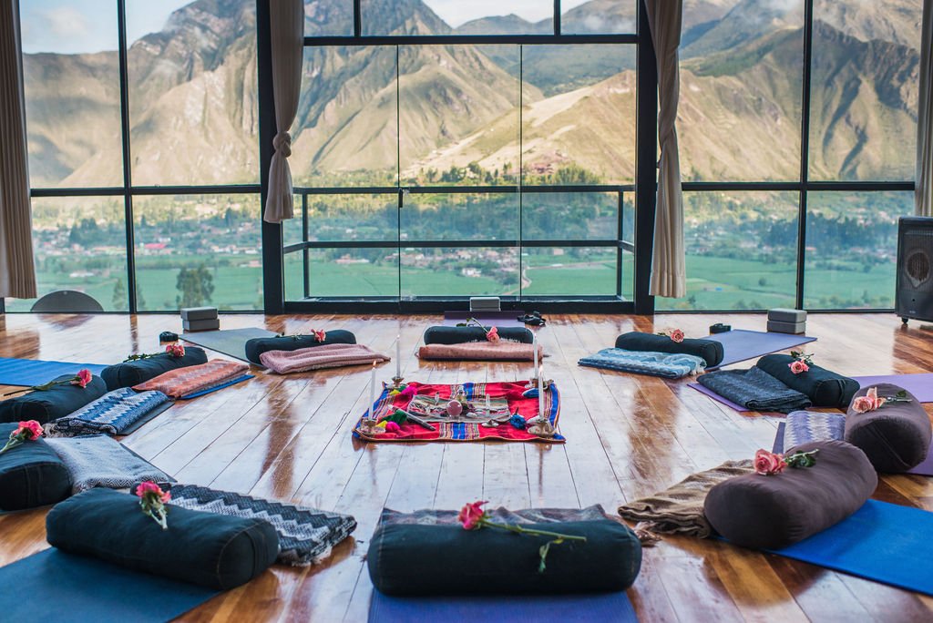 Yoga mats, bolsters, blankets, and roses are arranged in a circle in a studio with floor-to-ceiling windows overlooking the Sacred Valley and the Andes.