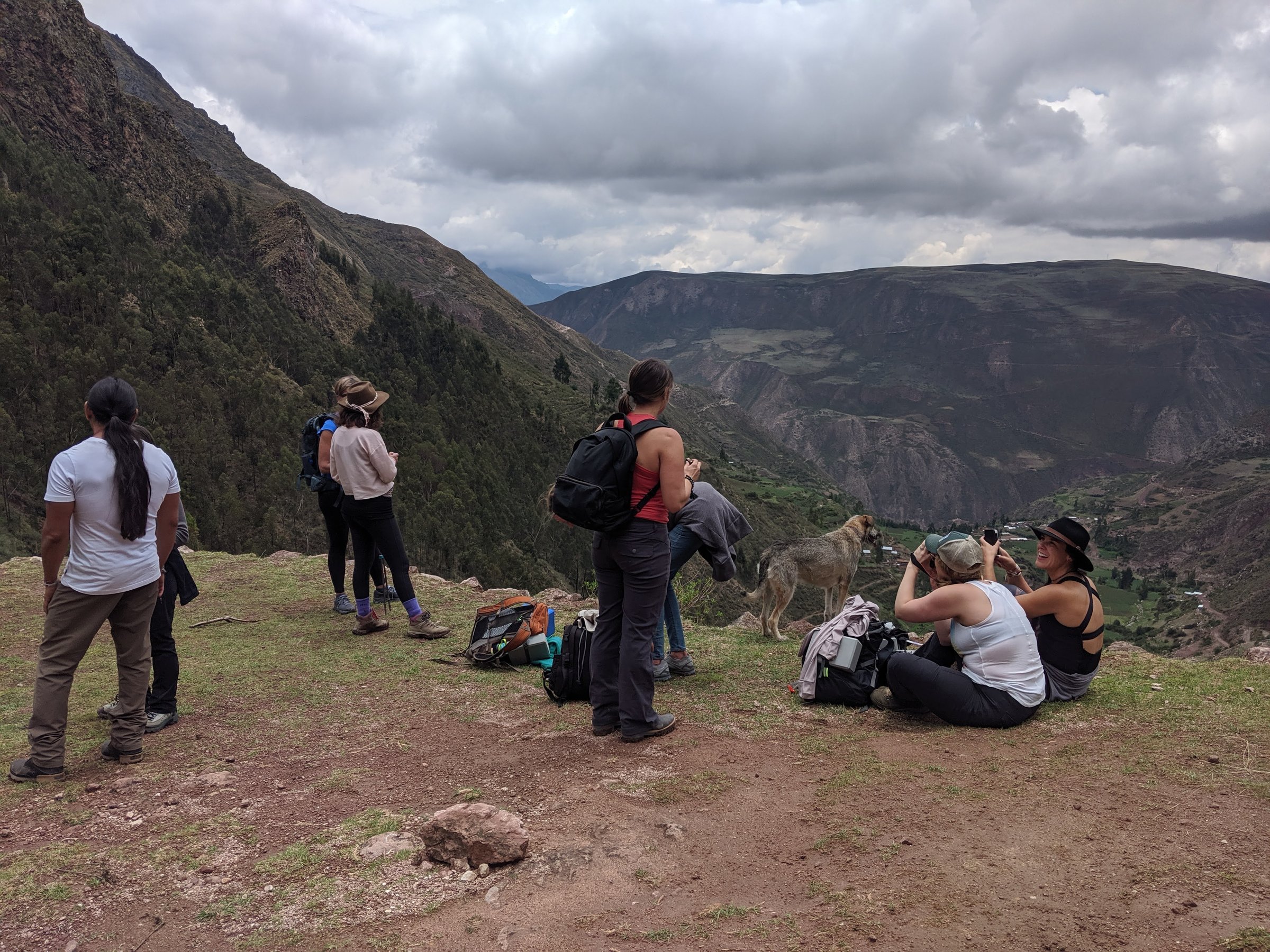A group of hikers and a dog pause on a high ridge to admire the cloud-covered vista of the Sacred Valley in the Peruvian Andes.